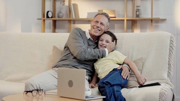 cheerful middle aged grandfather hugging happy grandson while watching movie at home - Φωτογραφία, εικόνα