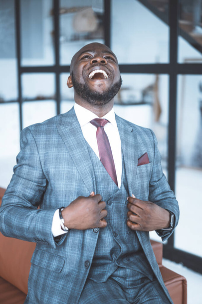 Successful Businessman in Formal Suit is Laughing with his Head Thrown Back. African Businessman Happy with a Successful Deal.Three-piece Suit. Close-up Portrait. Big Window Background  - Photo, Image