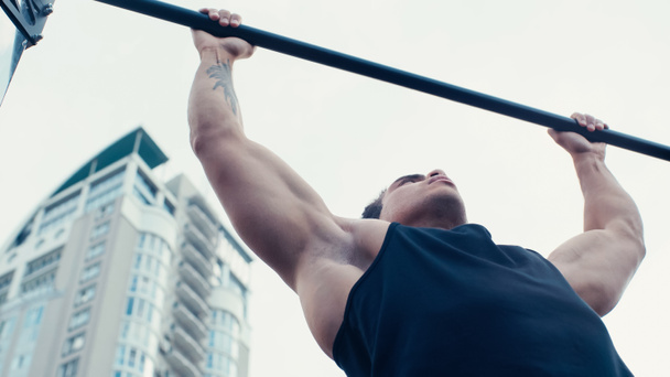 low angle view of tattooed mixed race man working out on horizontal bar outdoors - Foto, immagini