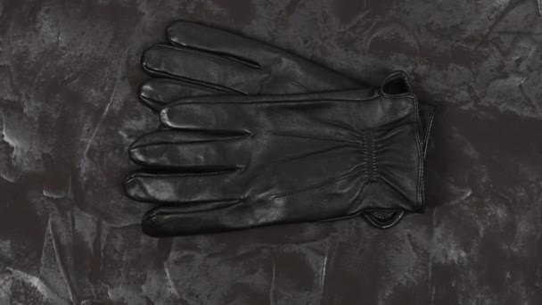 Schwarze Lederhandschuhe auf dunklem, strukturiertem Hintergrund. Ansicht von oben. 4K UHD Videomaterial 3840X2160. - Filmmaterial, Video
