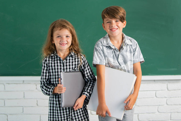 School children siblings hold book with surprising expression against blackboard. School kids friends. - Foto, Imagen