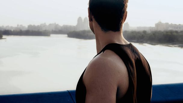 Sportlicher Mann steht auf Stadtbrücke über Fluss - Foto, Bild