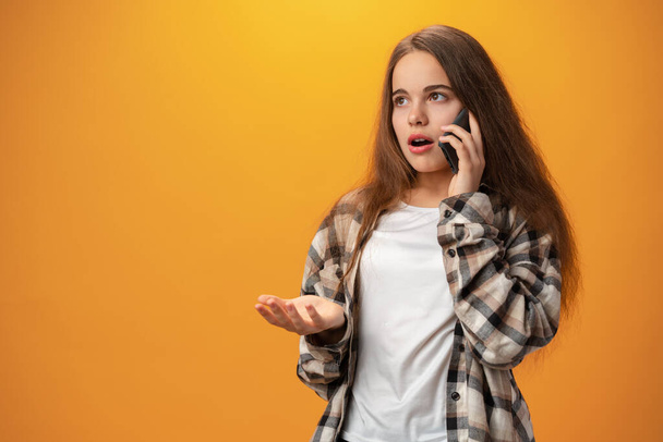 Pretty teenage girl talking on the mobile phone against yellow background - Foto, imagen