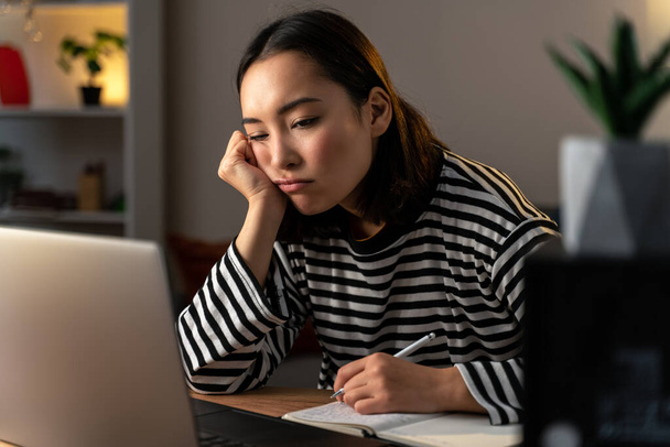 Mujer asiática sentirse cansado mientras se sienta delante de la computadora portátil y escribir algo durante el trabajo en la noche. Foto de stock - Foto, Imagen