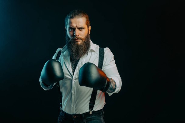 Serious beared man stands in boxing gloves wears in white shirt on a dark background in the studio. - Foto, Imagem