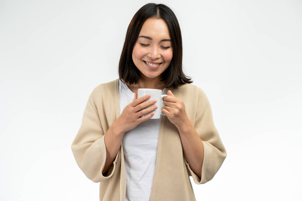 Widok pasa w górę portret azjatyckiej kobiety z krótkimi włosami trzymając filiżankę kawy izolowane na białym tle - Zdjęcie, obraz