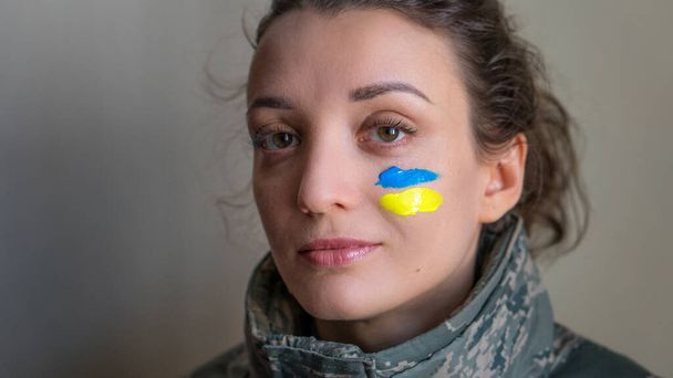 Sisäuima muotokuva nuori tyttö sininen ja keltainen ukrainalainen lippu poskellaan yllään sotilaallinen univormu, pakollinen asevelvollisuus Ukrainassa, tasa-arvon käsitteitä - Valokuva, kuva