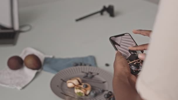 Μέση closeup αγνώριστη Αφρο-αμερικανική γυναίκα λήψη φωτογραφιών από νόστιμα blueberry τηγανίτες τυρί στο smartphone - Πλάνα, βίντεο