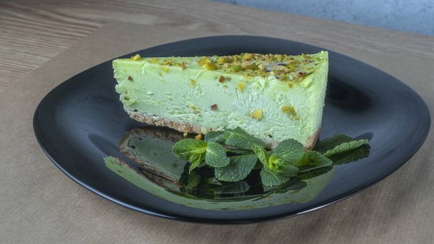 Close-up view of green pistachio cake with leaf of mint on black plate. Creamy pistachio cheesecake. Festive concepts. - Φωτογραφία, εικόνα