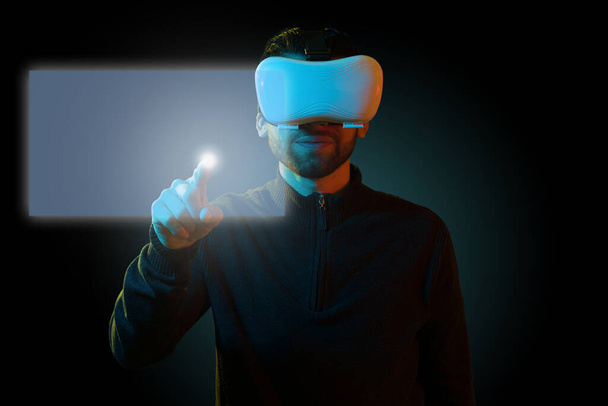 Υψηλή τεχνολογία. Νεαρός άνδρας με γυαλιά εικονικής πραγματικότητας που αγγίζει οθόνη ολογράμματος με επαυξημένη πραγματικότητα - Φωτογραφία, εικόνα