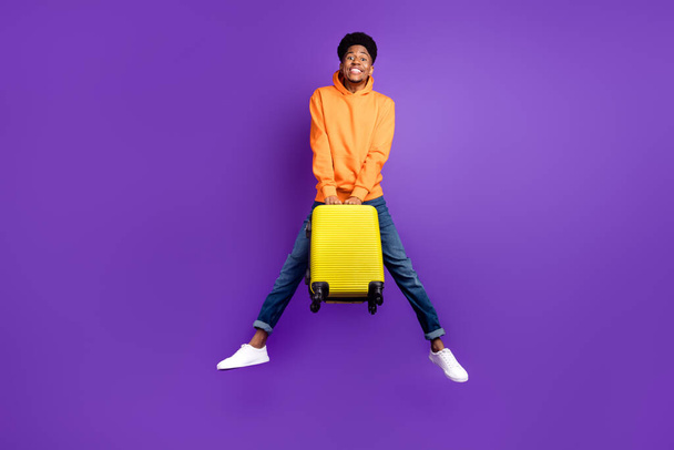 Full size photo of young black man happy positive smile jump hold suitcase travel vacation isolated over violet color background - Photo, Image