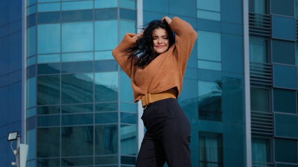 Happy carefree young woman brunette model actively dancing outdoors on city building background funny joyful hispanic girl student smiling rhythmically moving winner dance enjoying weekend freedom - Fotó, kép