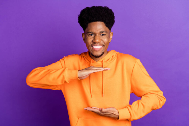 Photo of funky brunet millennial guy hands measure wear orange hoodie isolated on violet color background - Foto, afbeelding