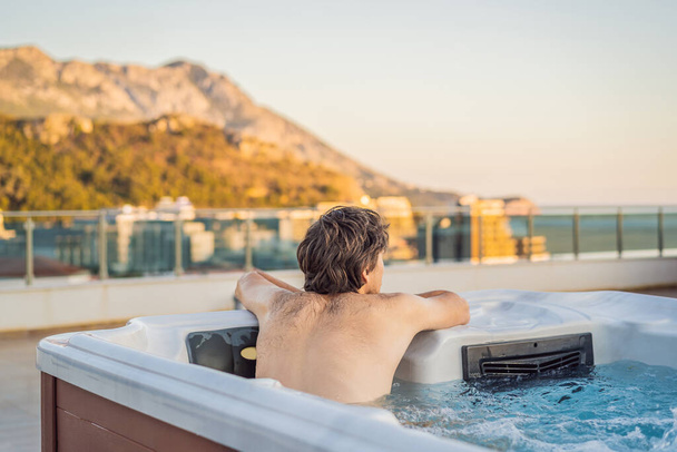 Portrait of young carefree happy smiling man relaxing at hot tub during enjoying happy traveling moment vacation life against the background of green big mountains - Foto, Imagen