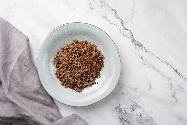 grey ceramic scandi soup bowl with traditional east european dish buckwheat on a marble surface and kitchen towel, top view, copy space - Fotó, kép
