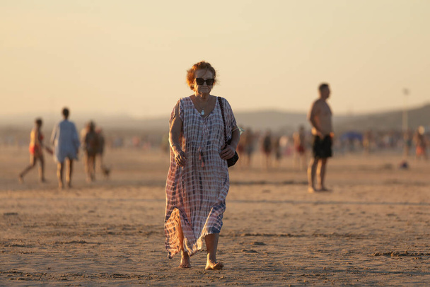 Zahara de los Atunes, Spain - Sept 03, 2021: An older adult woman walks alone on the beach at sunset, Cadiz province - Photo, Image