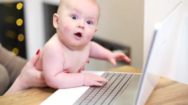 Mujer joven con niño pequeño en brazos escribiendo en el ordenador portátil, trabajo remoto con un bebé en casa. - Metraje, vídeo