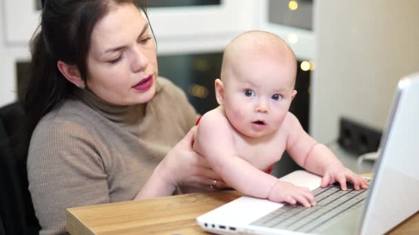 Young woman with toddler in arms typing on laptop, remote work with a baby at home. - Felvétel, videó