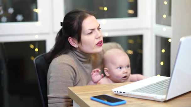Junge Frau mit Kleinkind im Arm tippt auf Laptop, Fernarbeit mit Baby zu Hause. - Filmmaterial, Video