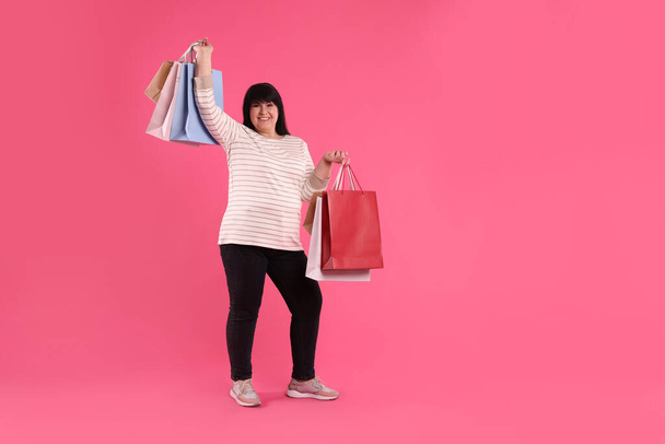 Beautiful overweight mature woman with shopping bags on pink background. Space for text - Fotoğraf, Görsel