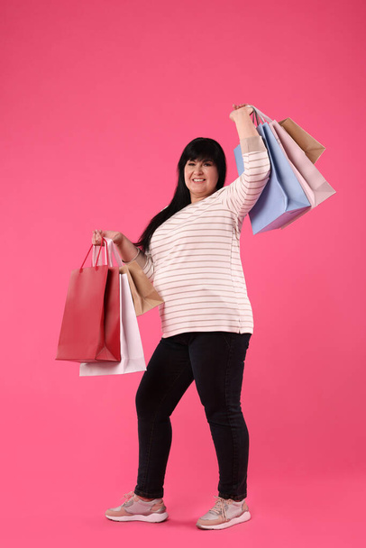Beautiful overweight mature woman with shopping bags on pink background - Φωτογραφία, εικόνα