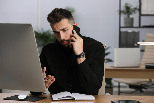 Homem falando ao telefone enquanto trabalhava na mesa no escritório - Foto, Imagem