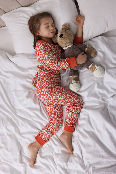 Cute little girl with toy bear sleeping on bed, top view - Foto, Bild