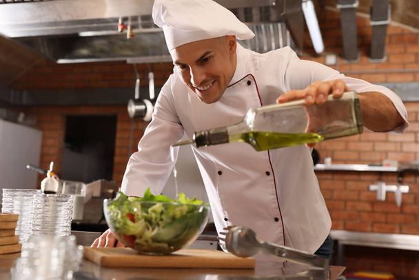 Professional chef pouring oil into bowl with fresh salad in restaurant kitchen - Zdjęcie, obraz