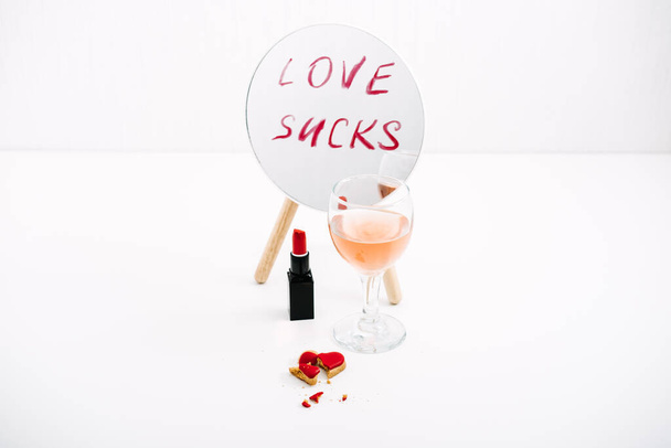 Broken heart, Divorce and relationship family breakdown. Loneliness, couple break up, divorce concept with red lipstick text Love Sucks on mirror, glasses of rose wine and broken heart candy. - Photo, Image