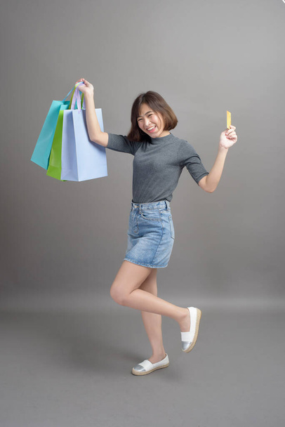 A portrait of young beautiful asian woman holding credit card and colorful shopping bag isolated over gray background studio - Fotografie, Obrázek