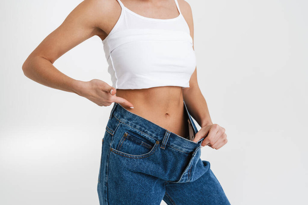 European woman pointing finger at her waist while posing in big jeans isolated over white background - Foto, immagini