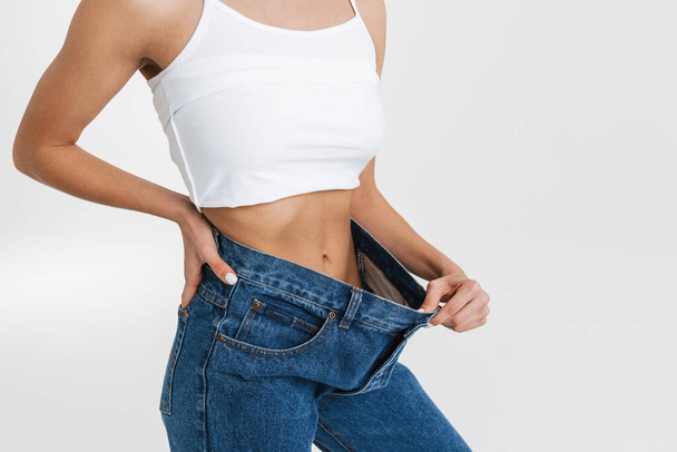 European woman showing her waist while posing in big jeans isolated over white background - Zdjęcie, obraz