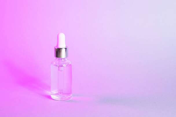 Facial serum in transparent glass bottle with dropper in pink neon gradient light. Cosmetic product for branding closeup. Trendy skin product advertising. Front view, copy space. - Foto, Bild