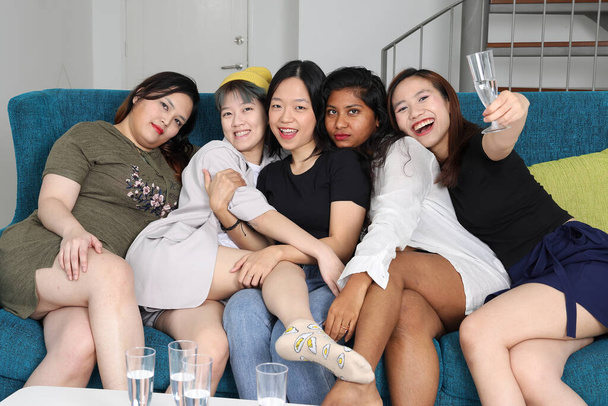 Giovane asiatico donna gruppo parlare gossip chat cantare bevanda applausi partito divertimento godere divertente volti espressione su blu soggiorno divano - Foto, immagini