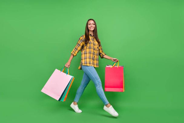 Full size profile portrait of cheerful positive girl hold packages walking isolated on green color background - Фото, изображение