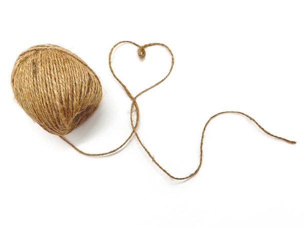 An unwound ball of thread, the thread forms a heart on a white background. Jute for gifts, souvenirs or flowers. - 写真・画像