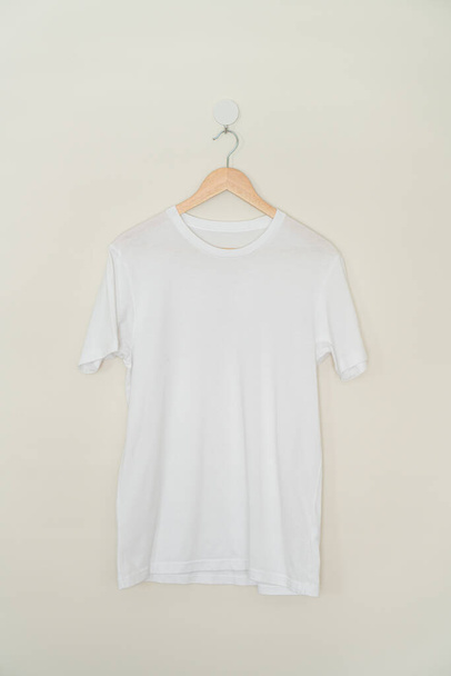 white t-shirt hanging with wood hanger on wall - Fotoğraf, Görsel