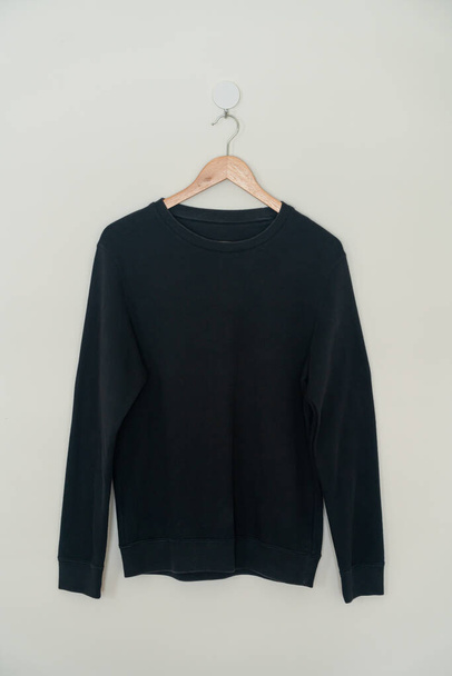 black sweater hanging with wood hanger on wall - Photo, image