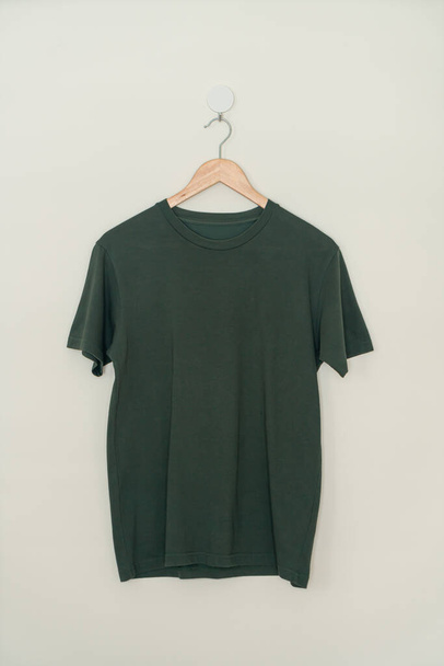 dark green t-shirt hanging with wood hanger on wall - Photo, image