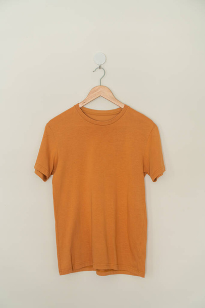 orange t-shirt hanging with wood hanger on wall - Foto, Bild
