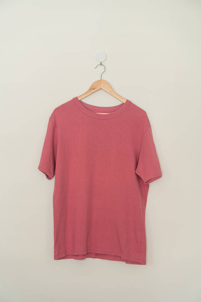 pink t-shirt hanging with wood hanger on wall - Fotó, kép