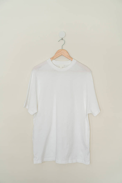 white t-shirt hanging with wood hanger on wall - Φωτογραφία, εικόνα