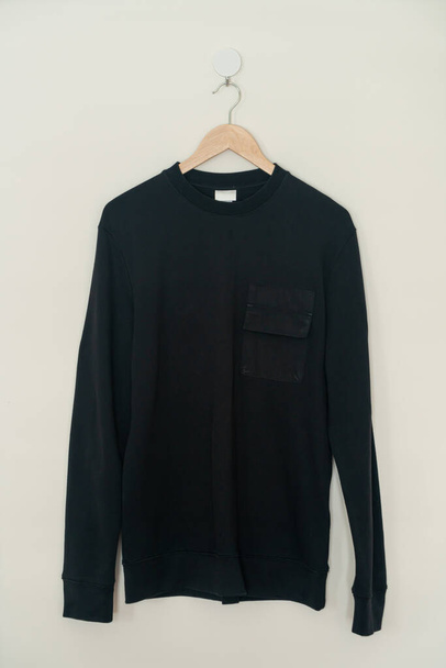 black sweater hanging with wood hanger on wall - Фото, зображення