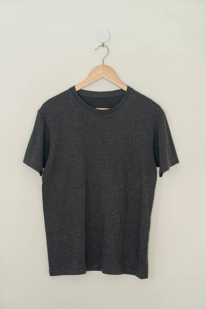 black t-shirt hanging with wood hanger on wall - Photo, Image