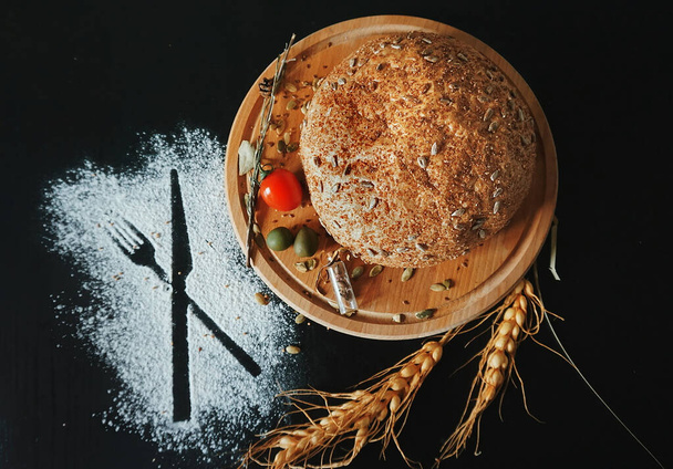 Pão redondo em uma tábua, trigo, farinha em uma mesa escura, vista superior. - Foto, Imagem