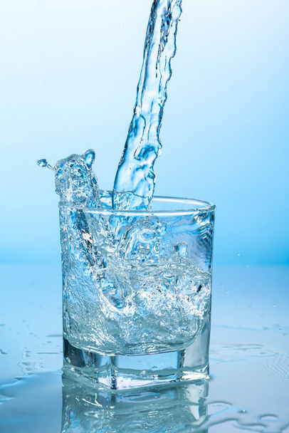 splash of water in a transparent glass on a blue background - Valokuva, kuva