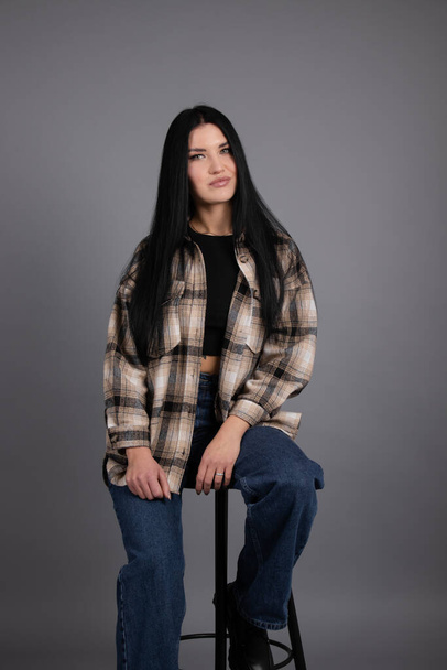 portrait of beautiful young woman in brown checkered shirt and jeans on gray background. pretty female portrait - Photo, image