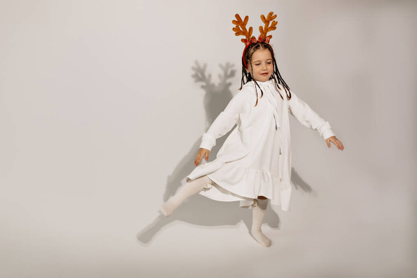 Full-lenght portrait of happy excited little girl with head accessory wearing white dress dancing and having fun over isolated background. High quality photo - Photo, image