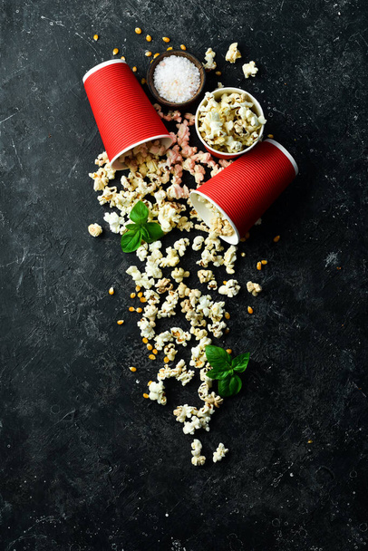 Salty popcorn in paper cups on a black stone background. Top view. - Foto, Imagen