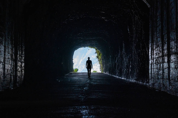 Silhouette of unrecognisable woman as she looks out from a dramatic tunnel in the old Sao Vicente road of the mountains of Madeira island. - Photo, Image